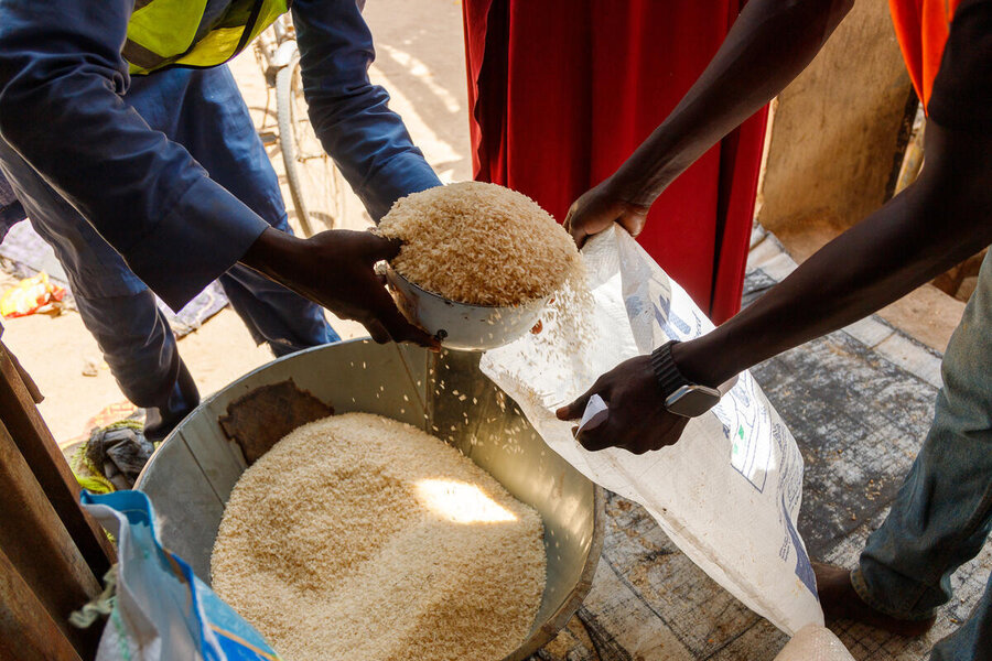 A closeup of a man scooping grains into a burlap bag held out by another man. Photo: WFP/Nommiyid Chantu