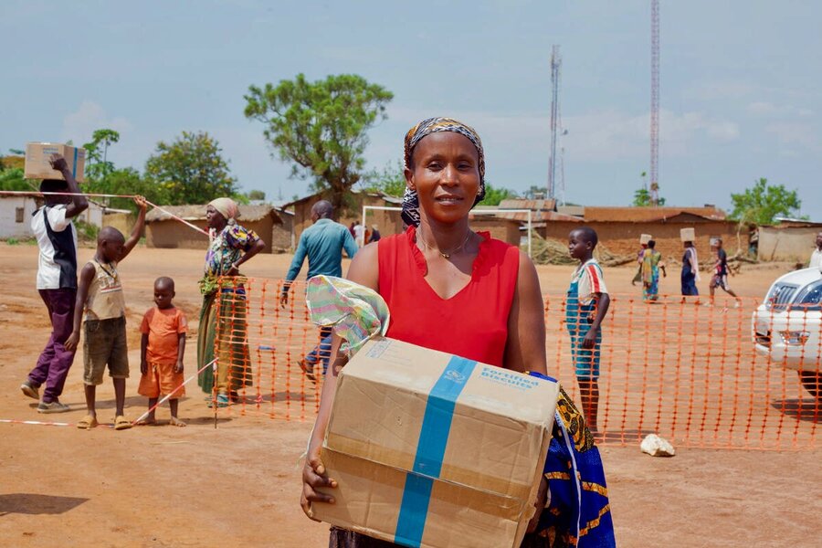A woman in a red sleeveless shirt carries a box of WFP high energy biscuits. Photo: WFP/Musa Abema
