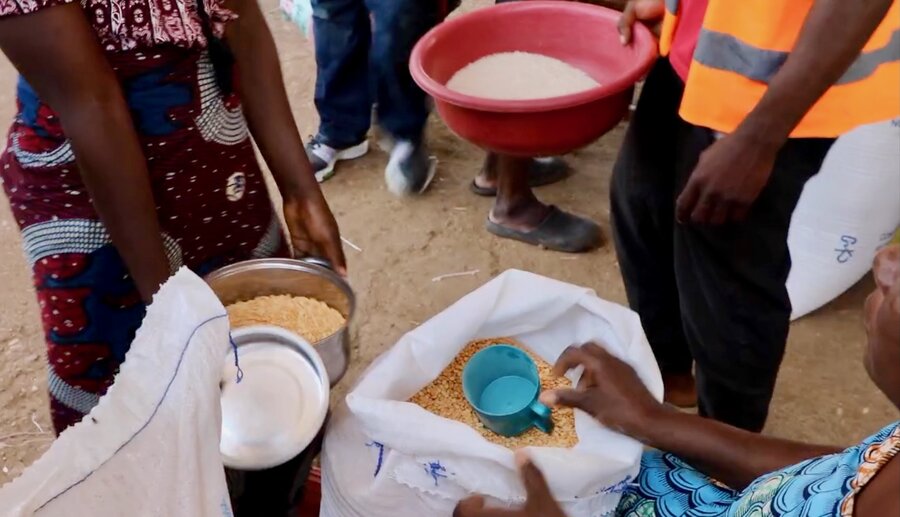 A closeup shot of a woman's hands scooping WFP food into a pot held by another woman. Photo: WFP/Irenee Nduwayezu