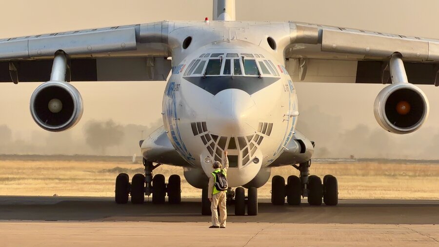 An aviation worker stands in front of a hulking cargo plane, giving directions. Photo: WFP/Hedley Tah 