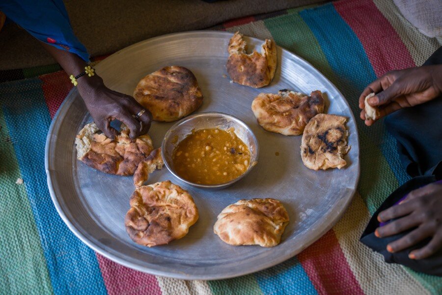 A closeup of a tray of flatbread and sauce, with hands dipping into it. Photo: WFP/Abubakar Garelnabei