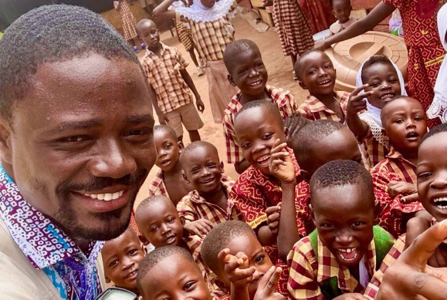 A headshot of a smiling man with a crowd of grinning children behind him. Photo: WFP/Abdul-Wahab Mohammed