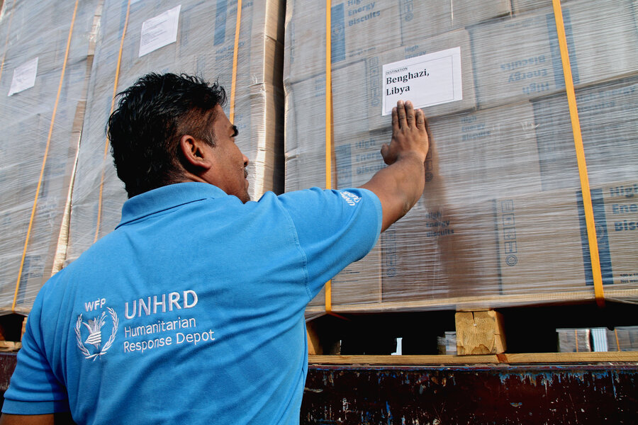 A WFP employee wearing a blue WFP UN Humanitarian Response Hub T-shift sticks a sticker on cargo indicating it's bound for Libya. Photo: WFP/Peppino Circa 