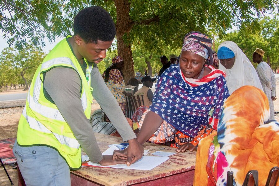 A woman in a colourful headscarf and shawl inks her name to a ledger documenting she's receiving WFP food assistance. Photo: WFP/Joseph Fambove