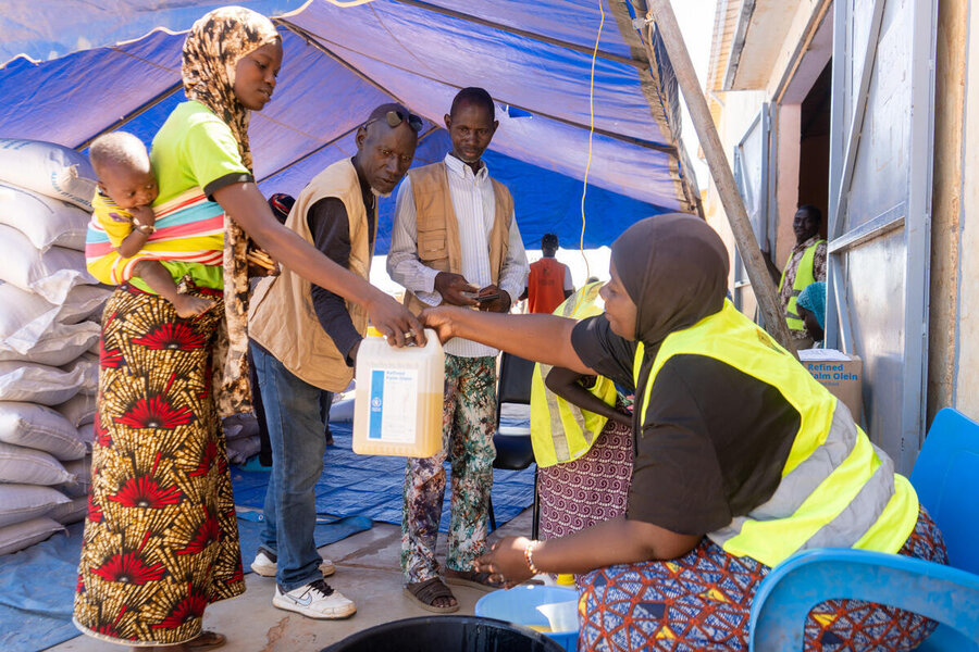 A woman with her baby strapped to her back receives WFP food assistance in a tent. Photo: WFP/Jecuthiel Yameogo