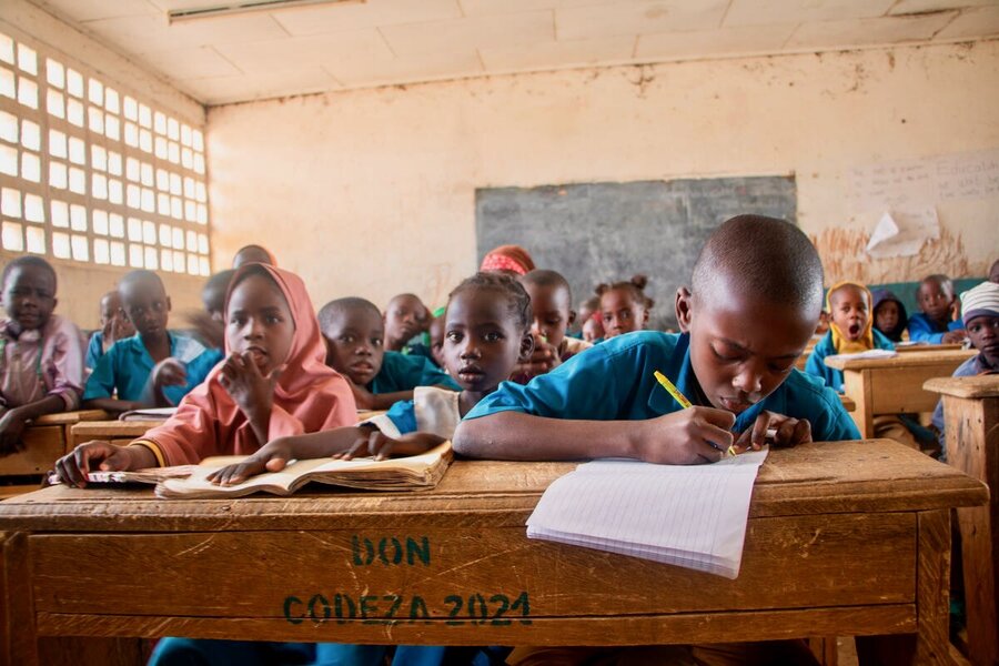 Small children listening and writing in a classroom with wooden benches and tables in northern Cameroon. Photo: WFP/Joseph Fambove