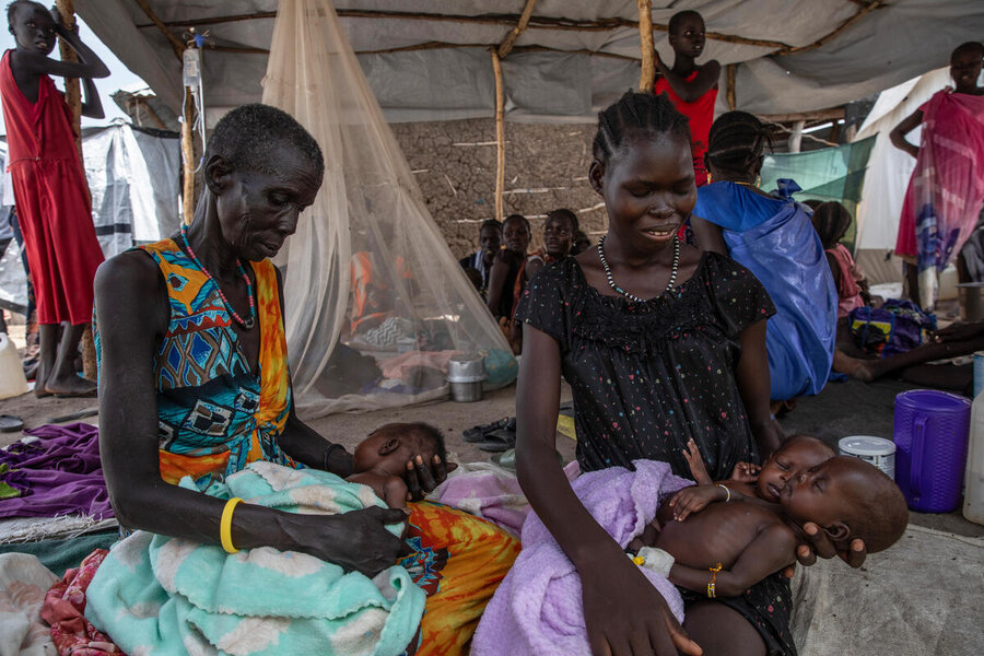 Two women cradle three small babies wrapped in brightly coloured blankets at a crowded health clinic. Photo: WFP/Gabriela Vivacqua