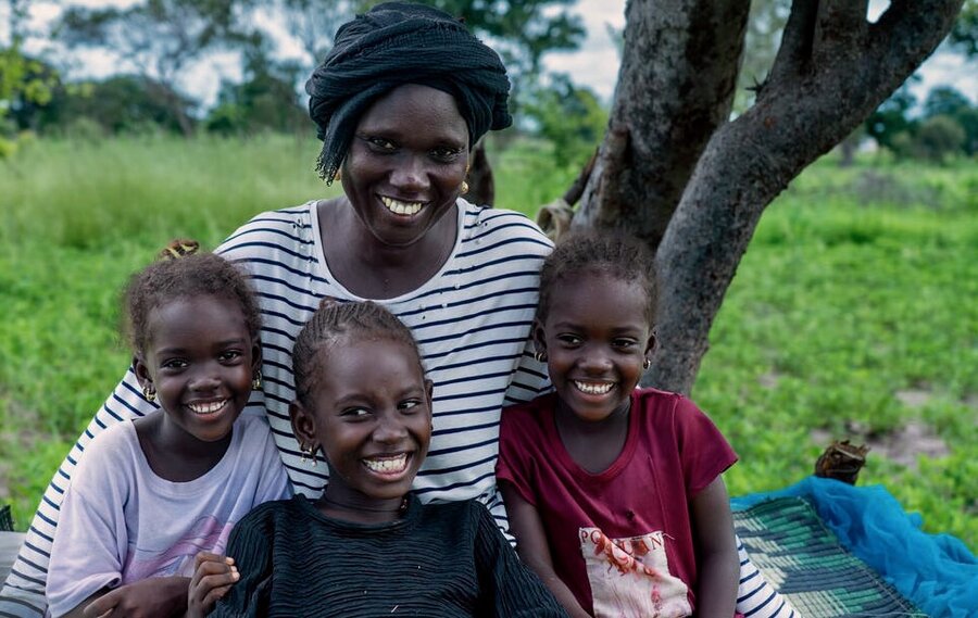 A smiling women hugs her three children as they pose for a photo backdropped by trees and a field. Photo: WFP/Sylvie Njobati