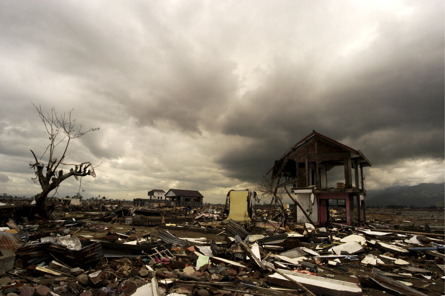 Storm clouds loom over a devastated settlement, with scattered debris, damaged houses and a lone standing structure amid widespread destruction.