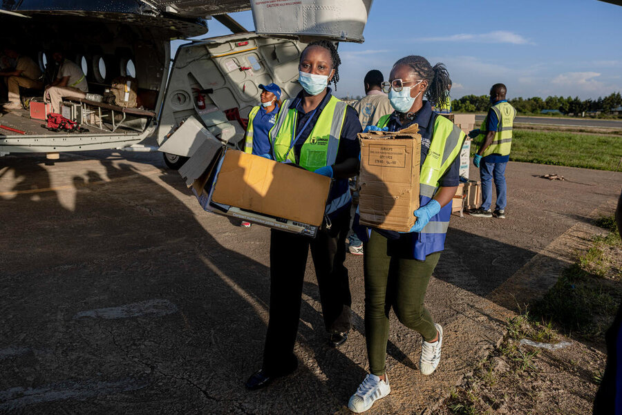 Humanitarian workers in reflective vests unload boxes from a cargo plane on a runway, carrying supplies for distribution under clear sky.