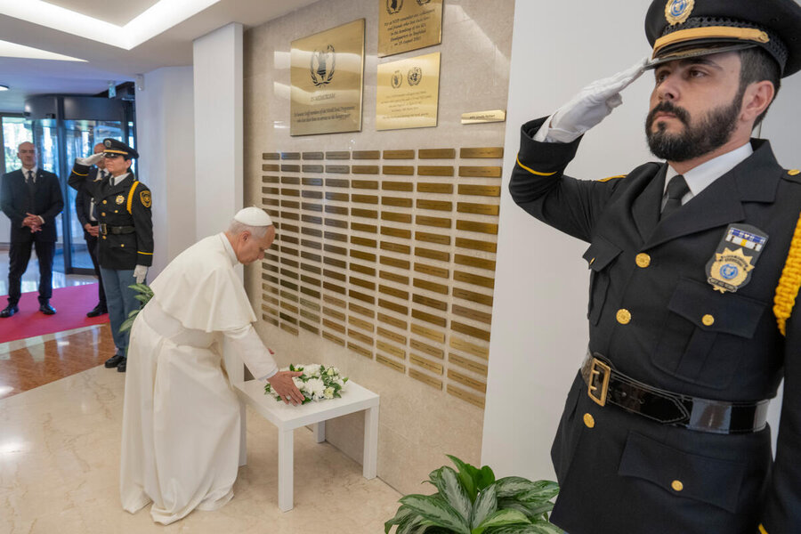 ReligiousPope lays white flowers at memorial wall as uniformed guards stand and salute in an hallway with marble floors.