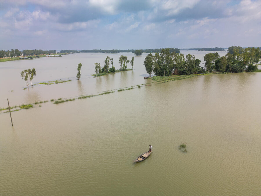 A small wooden boat in a wide, flooded river with a few trees sprouting out of the water. Photo: WFP/Mehedi Rahman