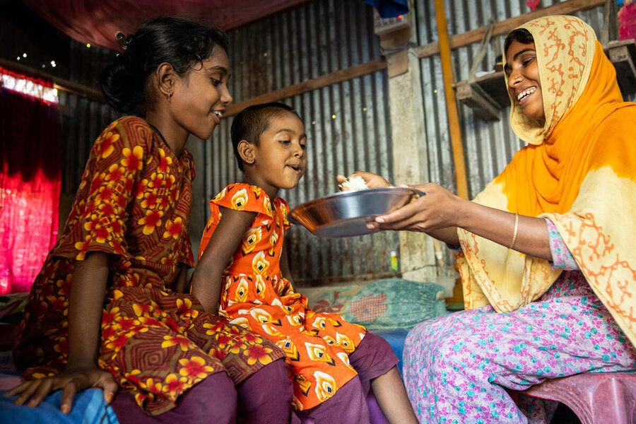 A smiling woman in a long scarf and robe feeds her two daughters oyster mushrooms from a bowl. Photo: WFP/Samantha Reinders