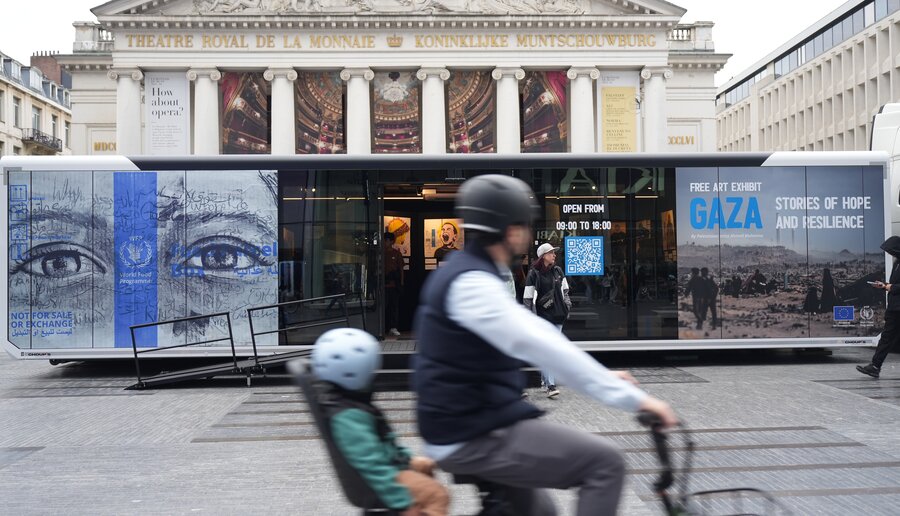 A biker, with a small child in the back, whizzes past a large poster of a Gaza exhibit on a public space. Photo: WFP