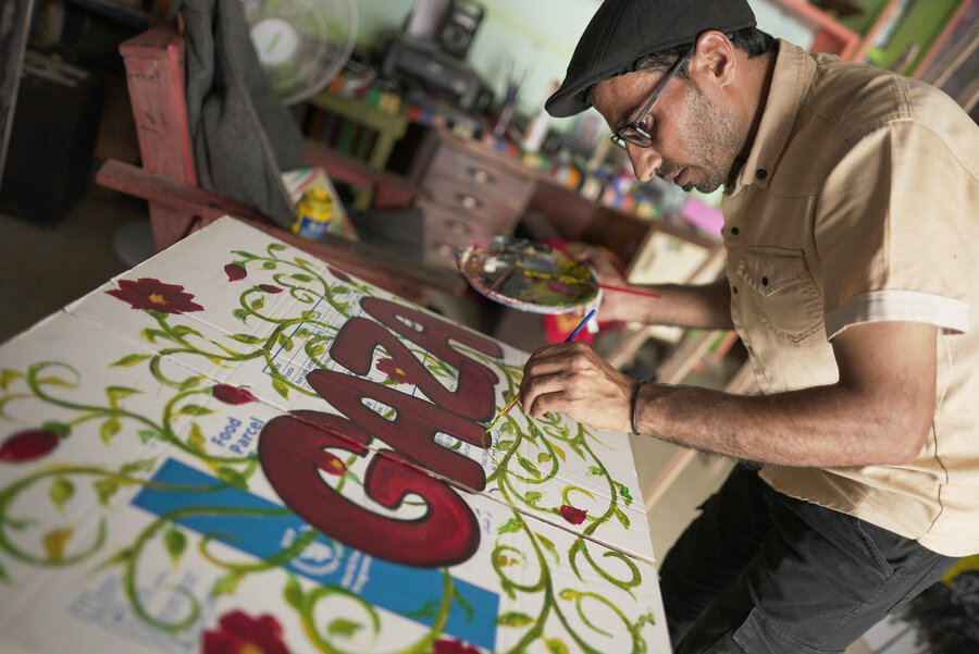A man in a beret paints a painting with the words "Gaza" on a WFP food box serving as a canvas. Photo: WFP