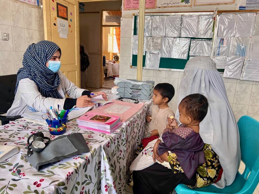 A woman in a light grey burka and two small children consults with a health care worker at a clinic. Photo: WFP/Isheeta Sumra