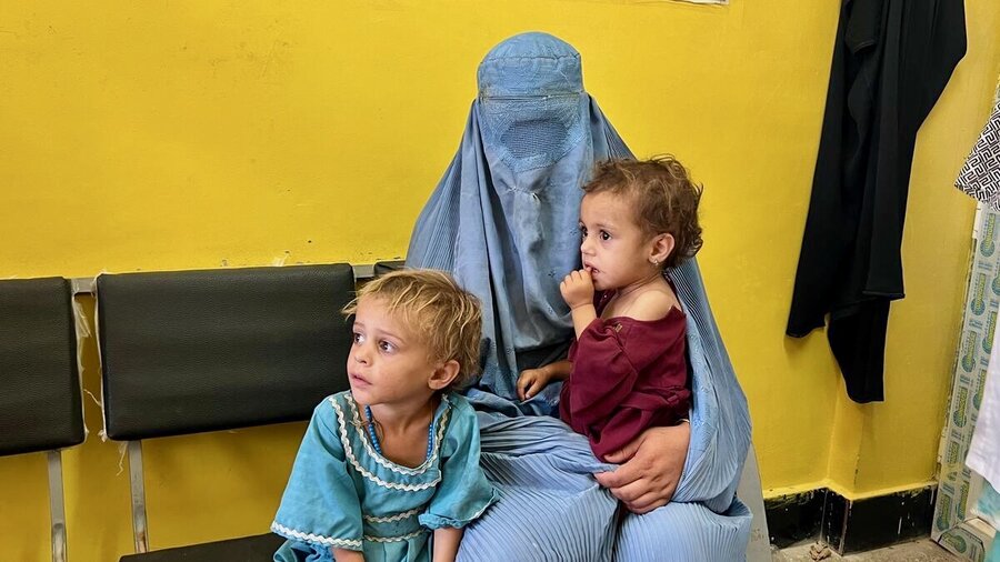 A woman wearing a light blue burka sits in a waiting room with two small children. Photo: WFP/Isheeta Sumra