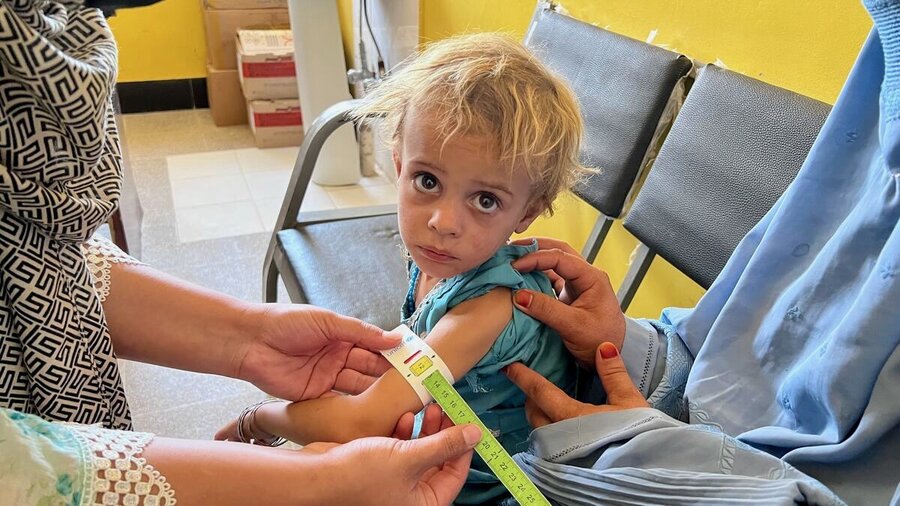 A little Afghan girl in an aqua-colored dress and blond hair is tested for malnutrition. Photo: WFP/Isheeta Sumra