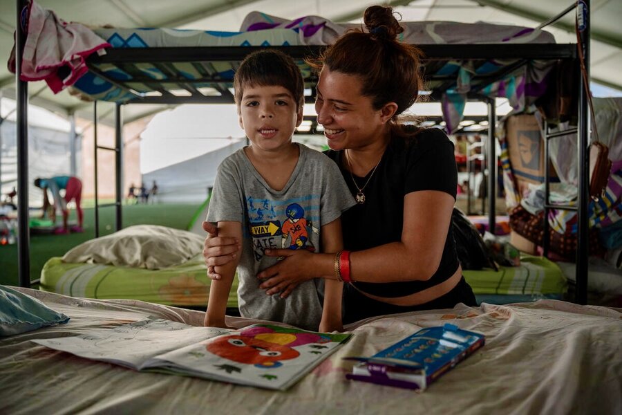 A smiling woman  wraps her arms around her young son as they sit at a table in a makeshift shelter. Photo: WFP/Gustavo Vera