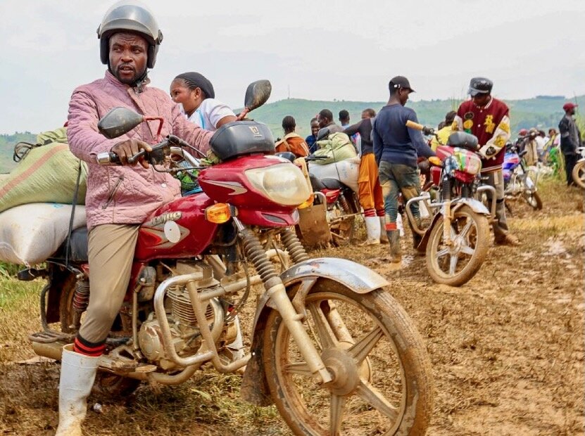 A man in a pink jacket sits on a motorcycle piled with bags of WFP food. Photo: WFP/Charly Kasareka