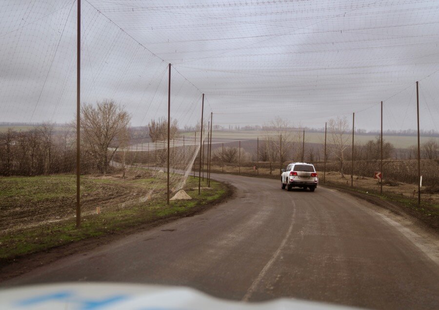 The front of a white vehicle seen from inside the car, with another farther away down a road covered with anti-drone nets. Photo: WFP/Sayed Asif Mahmud