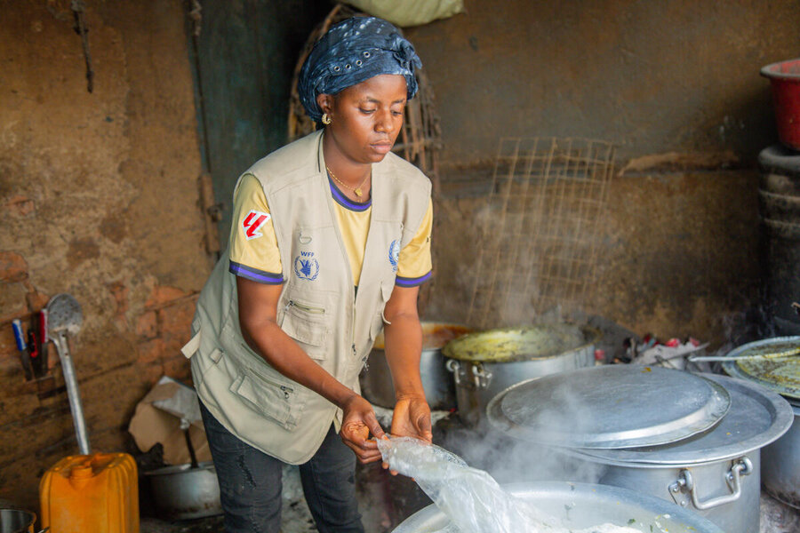 A woman wearing a headscarf and tan WFP jacket stirs a large pot of cooking food. Photo: WFP/Arete/Seros Muyisa