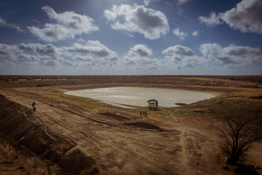 A large waterpan, or water catchment system, under a blue sky dotted with clouds, and surrounded by dry land.  Photo: WFP/Dennis Matendechere