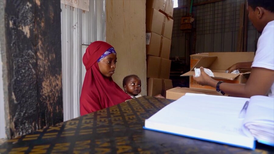 A woman in a red headscarf holding a small child picks up WFP's fortified nutritional supplements from a health worker outside Mogadishu, Somalia. The support may end in October for lack of funds. Photo: WFP/Sylvie Njobati