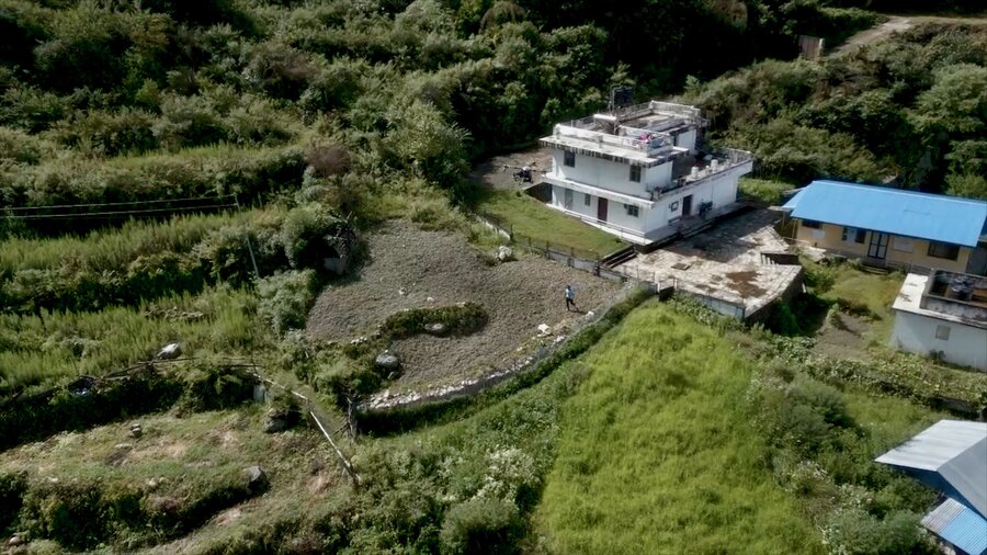A drone hovers over buildings and fields as a man below retrieves bags of WFP food assistance. Photo: WFP