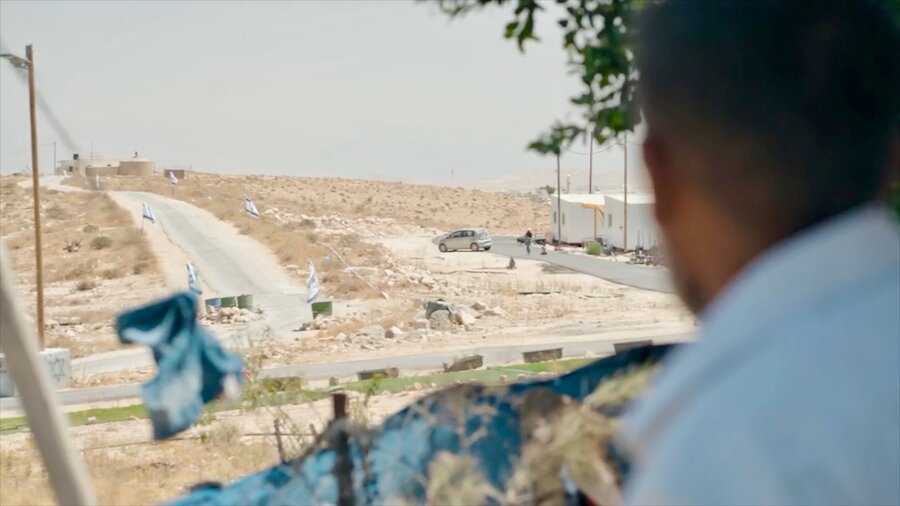 The back of a Palestinian man looking out at white temporary caravans an Israeli West Bank settlers. Photo: WFP/Hugh Rutherford