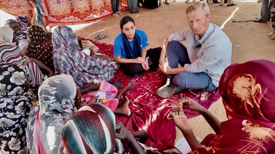 A man in jeans and woman (latter wearing a WFP T-shirt) speak to conflict-displaced women in Sudan. Photo: WFP