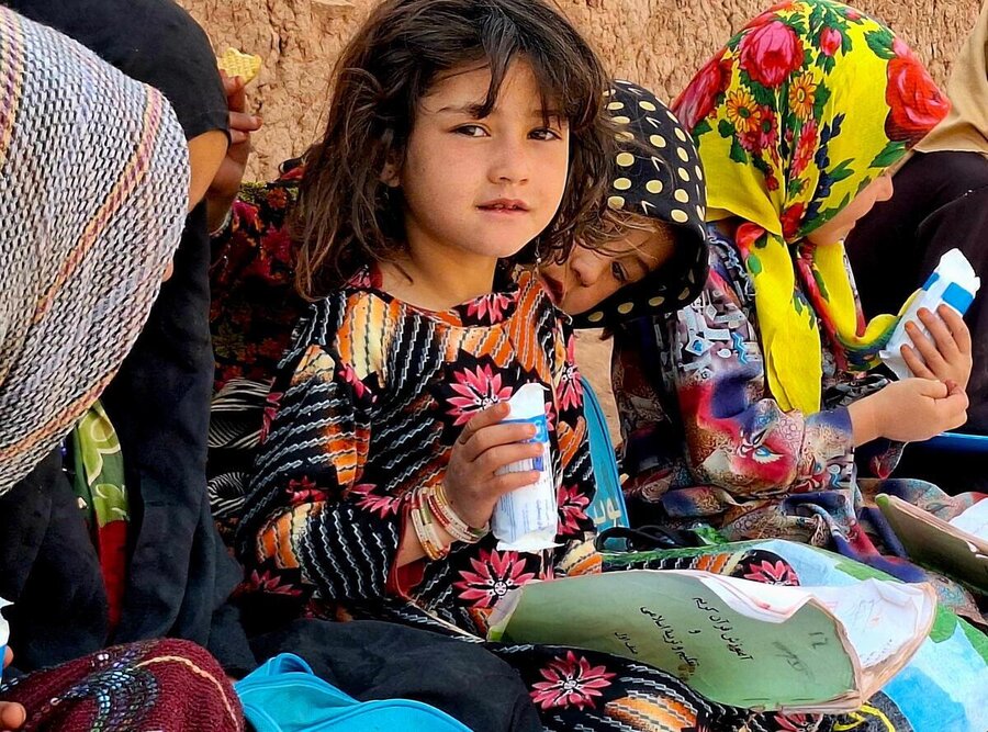 Afghan primary school girls in colorful dresses and headscarves eat WFP's fortified biscuits. Photo: WFP/Parviz Zahed