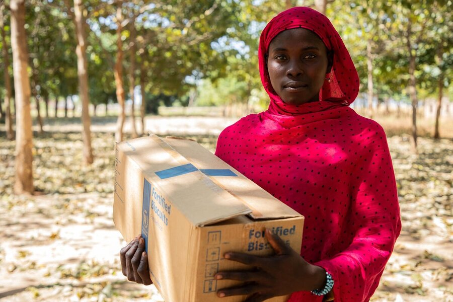 Person carrying a box of fortified biscuits in a wooded outdoor area, holding food assistance supplies distributed to support vulnerable communities.