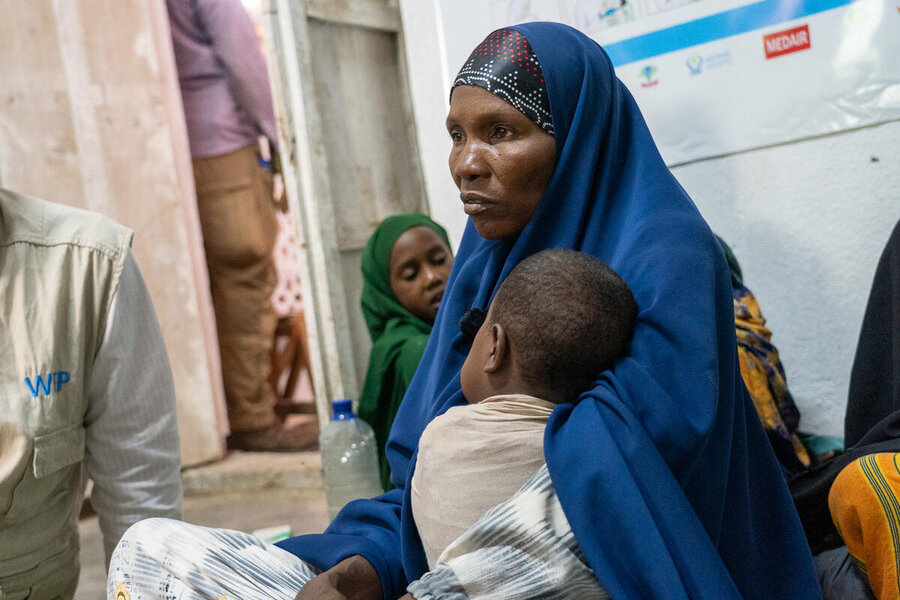 A woman wearing a dark blue scarf cradles a small child as she awaits for nutrition support in Somalia. Photo: WFF/Sara Cuevas Gallardo 