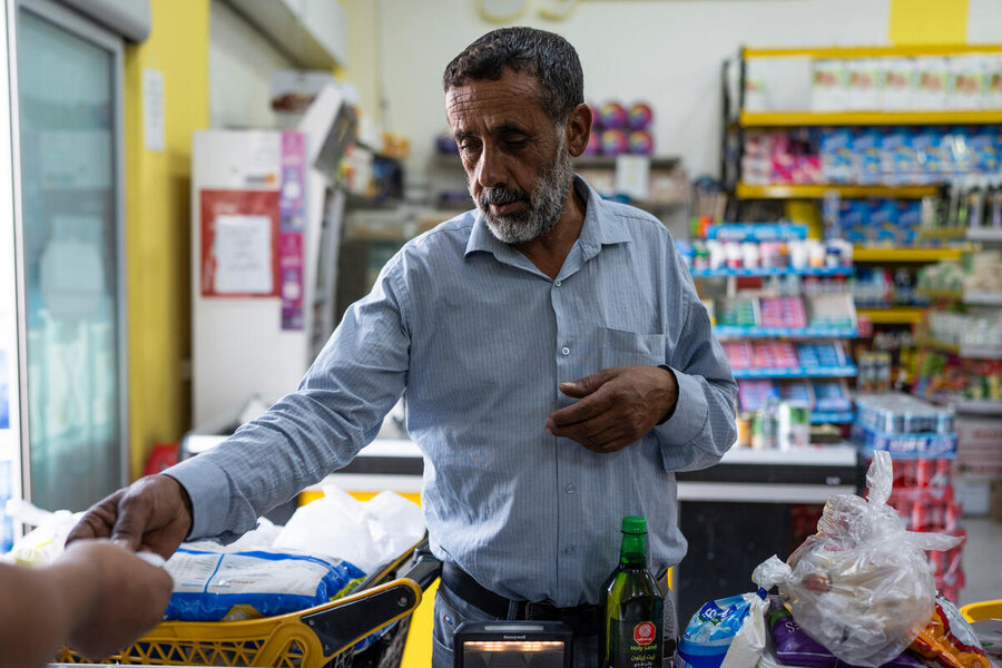 A man with a grey beard, short hair and a blue shirt buys food items with WFP cash assistance at a store. Photo: WFP/Hugh Rutherford