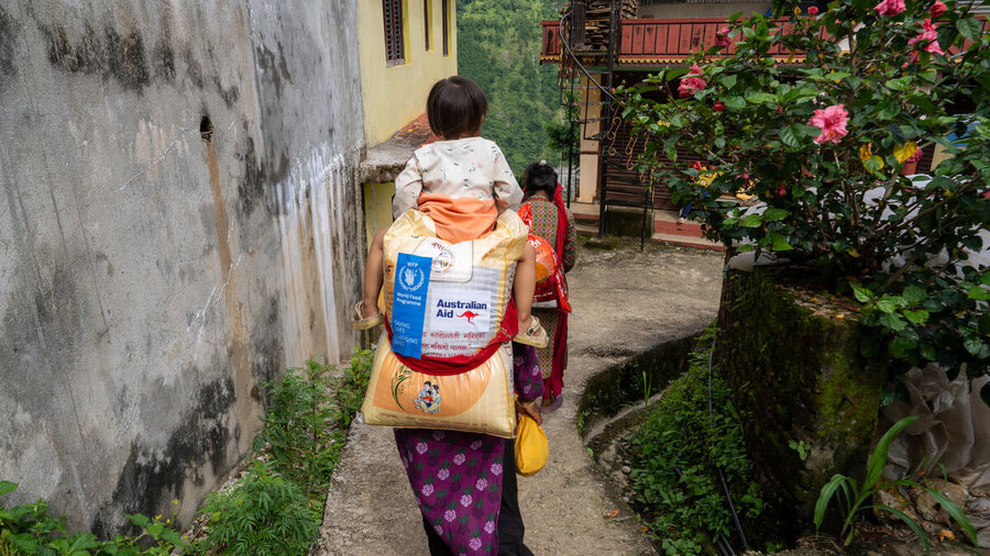 The back of a woman with a child on her head and WFP food bag with an Australian aid logo on her back. Photo: WFP/Shrawan Shrestha