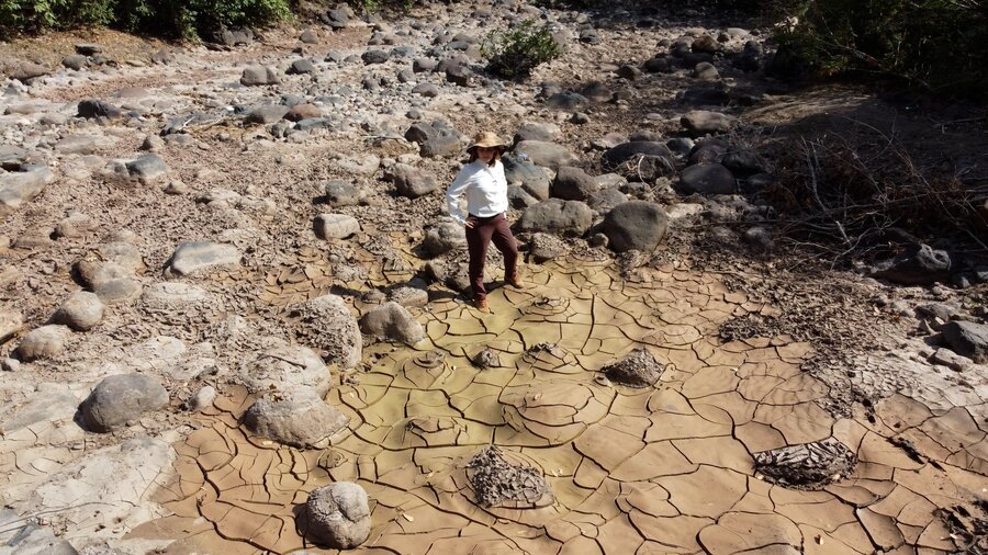 A women in a cowboy hat and brown pants surveys a dried-up water body. Photo: WFP/Darlan Bautista  