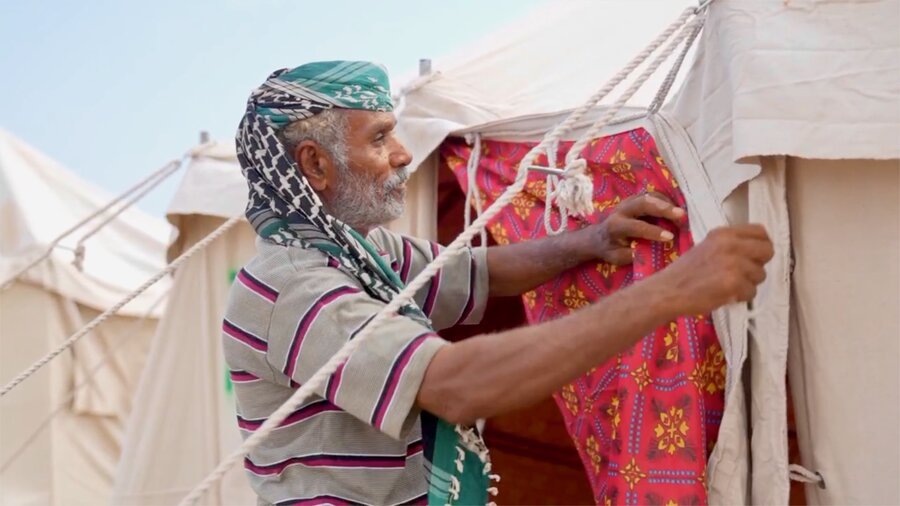 A man in a grey striped T-shirt and scarf around his head fixes a tent at a displacement camp in the Yemeni city of Aden. Photo: WFP
