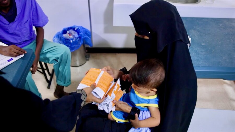 A woman in a black niqab holds a child, as she receives WFP nutritional assistance in Djibouti. Photo: WFP/Viktor Presenti