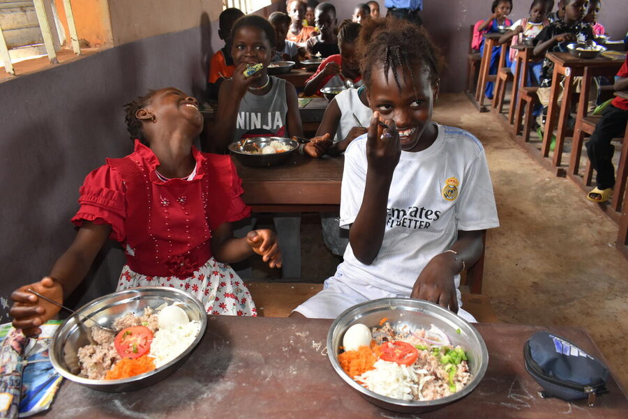 Children laughing in a classroom as they eat hearty plates of food. Photo: WFP/Isabel Correia