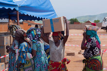 Photo: WFP/Musa Abema. a woman, having just received assistance, carries a box of biscuits on her head, Sange, Uvira Territory, South Kivu Province, DRC.