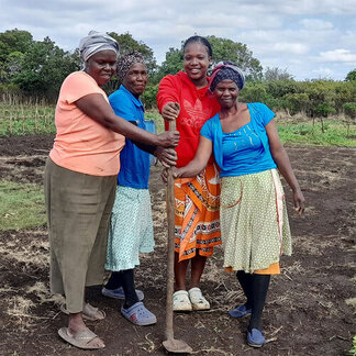 Four women are holding a shovel in a field