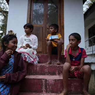 Children sitting on the steps of a building, some holding food items, sharing an outdoor moment.