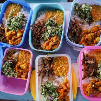 Colourful meal containers filled with rice, lentil curry, sautéed vegetables, and leafy greens arranged on a table.