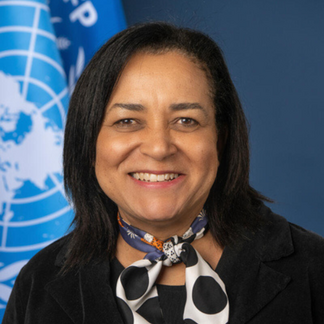 A portrait of WFP's Chief of Staff a.i. Valerie Guarnieri, standing in front of blue flags representing WFP and the United Nations.