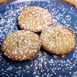 A plate of three round mopane muffins dusted with powdered sugar sits on a blue ceramic plate. The muffins are golden brown and arranged on a woven placemat, showcasing a nutritious recipe made with locally available ingredients.