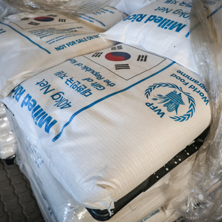 Stacked bags of fortified milled rice marked with WFP and donor branding, arranged on pallets in a storage or distribution area.