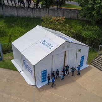 Aerial view of a white WFP tent with blue-shirted staff in masks outside, set in a green area with steps and trees.