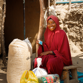A portrait of Falmata, (20) showing food items she received from WFP general food assistance via e-vouchers delivered as cash-based transfers to her SCOPE card and purchased at a WFP retailer in her community.
