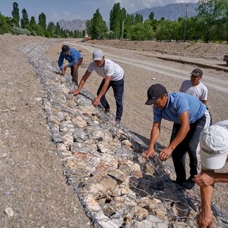 Men put barbed wire netting on rocks lining a road under construction. Photo: WFP